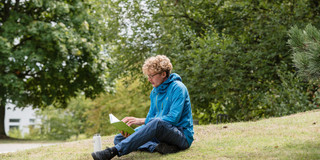 Student on meadow A student sits on a meadow and reads in a book.